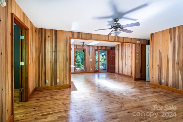 unfurnished room with wood-type flooring, wooden walls, and ceiling fan