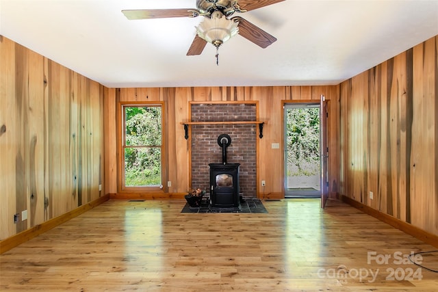 unfurnished living room with ceiling fan, light wood-type flooring, wood walls, and a wood stove