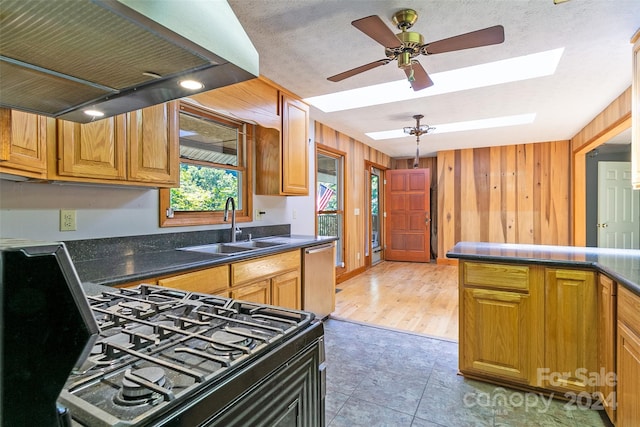 kitchen featuring ceiling fan, a skylight, wood walls, light hardwood / wood-style flooring, and dishwasher