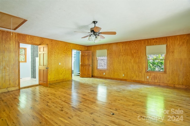 spare room featuring light hardwood / wood-style flooring, wood walls, ceiling fan, and a healthy amount of sunlight