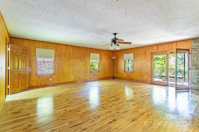 spare room with light hardwood / wood-style flooring, a wealth of natural light, ceiling fan, and wooden walls