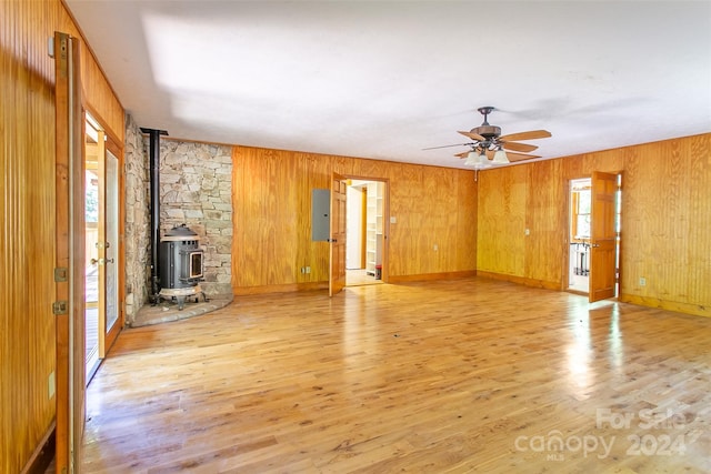 unfurnished living room with ceiling fan, wooden walls, light wood-type flooring, and a wood stove