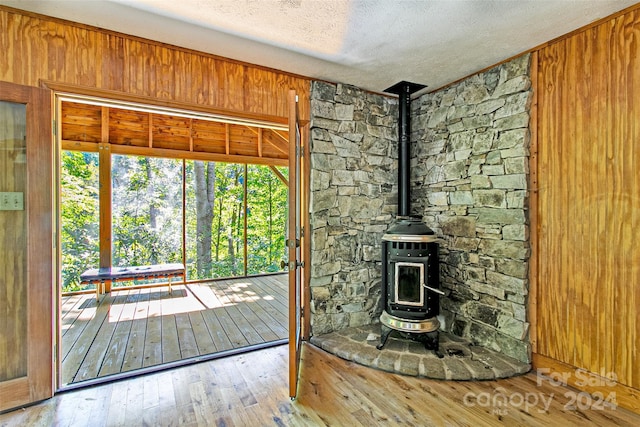 unfurnished living room featuring a textured ceiling, wood walls, a wood stove, and hardwood / wood-style flooring