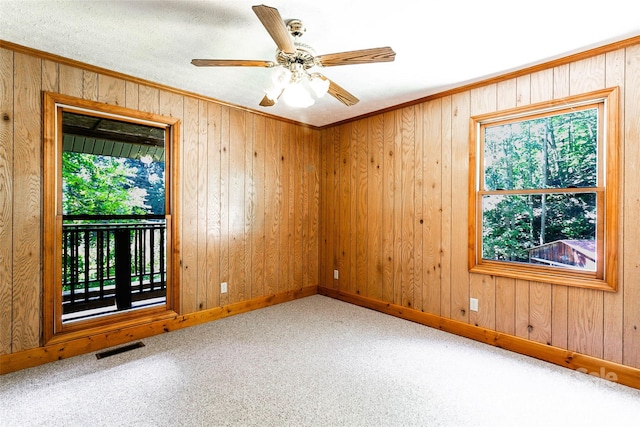 carpeted empty room featuring wood walls, ceiling fan, and crown molding