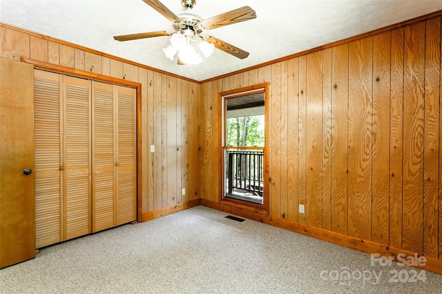 unfurnished bedroom with ornamental molding, wooden walls, ceiling fan, and light colored carpet