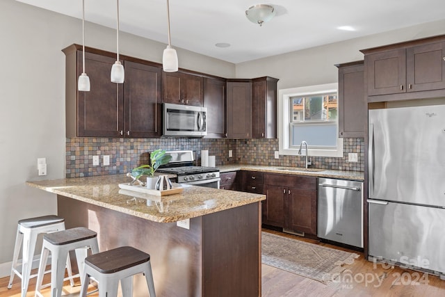 kitchen with kitchen peninsula, a kitchen breakfast bar, stainless steel appliances, sink, and light hardwood / wood-style flooring