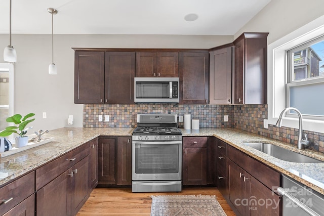 kitchen featuring sink, light wood-type flooring, appliances with stainless steel finishes, decorative light fixtures, and light stone counters