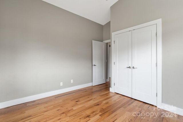 unfurnished bedroom featuring light wood-type flooring, high vaulted ceiling, and a closet