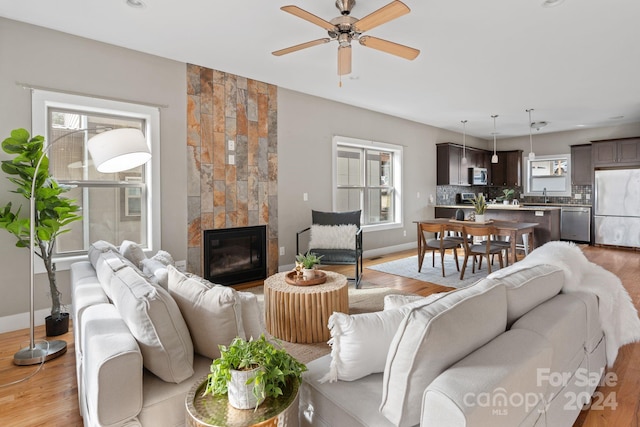 living room featuring ceiling fan, light wood-type flooring, sink, and a tiled fireplace