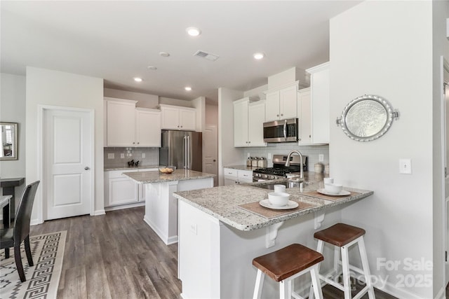 kitchen with appliances with stainless steel finishes, white cabinetry, tasteful backsplash, kitchen peninsula, and light stone counters