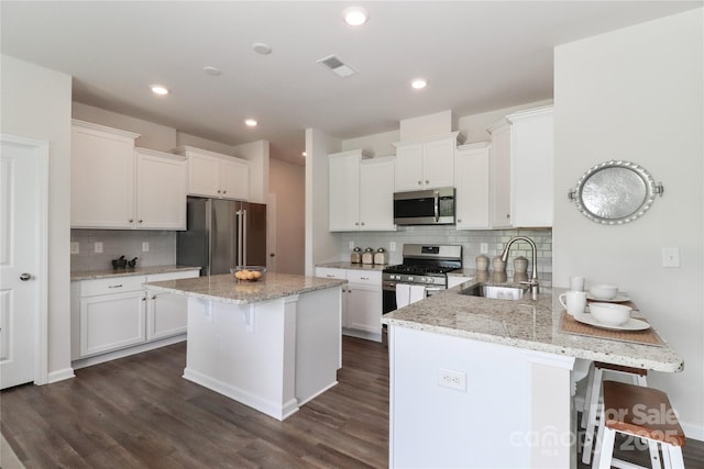 kitchen featuring white cabinets, appliances with stainless steel finishes, a kitchen bar, sink, and kitchen peninsula