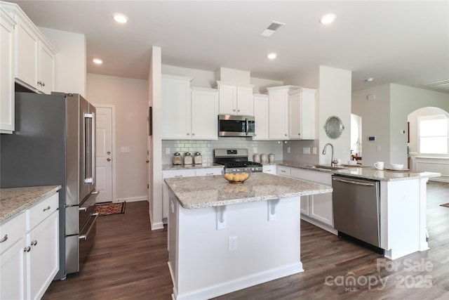 kitchen with light stone countertops, stainless steel appliances, white cabinets, and a center island