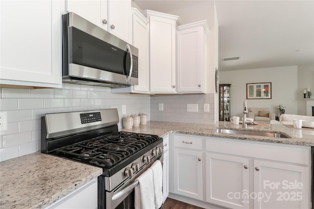 kitchen featuring backsplash, sink, appliances with stainless steel finishes, white cabinets, and light stone counters