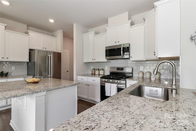 kitchen with white cabinets, appliances with stainless steel finishes, decorative backsplash, sink, and light stone counters