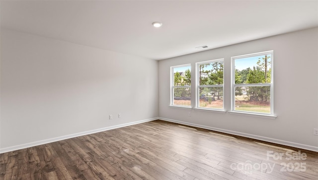 spare room featuring wood finished floors, visible vents, and baseboards