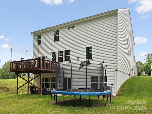 rear view of property with a trampoline, a deck, a yard, and central AC unit