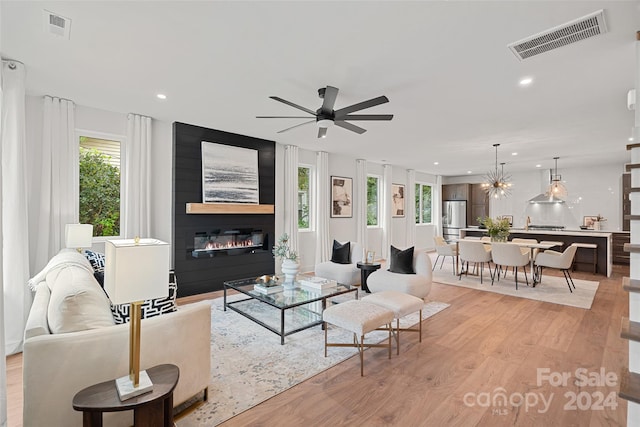 living room featuring ceiling fan, a large fireplace, and light hardwood / wood-style flooring