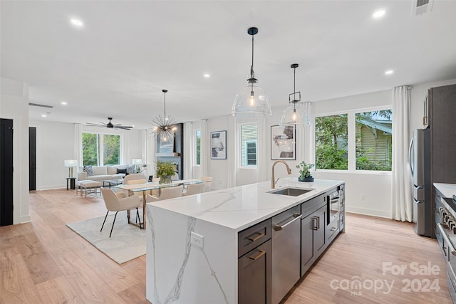 kitchen featuring a center island with sink, sink, light stone countertops, light wood-type flooring, and appliances with stainless steel finishes