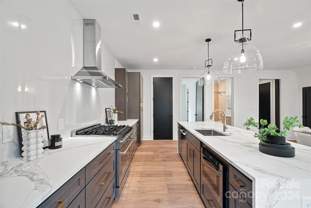 kitchen with light hardwood / wood-style floors, sink, wall chimney exhaust hood, decorative light fixtures, and stainless steel stove