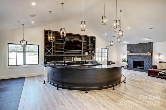 bar with hanging light fixtures, a fireplace, light hardwood / wood-style flooring, and high vaulted ceiling