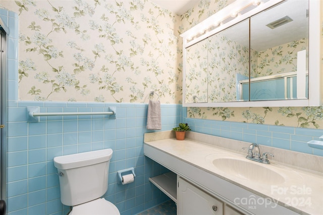 bathroom featuring tile walls, vanity, toilet, and a shower with shower door