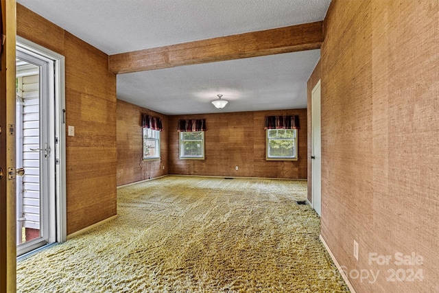 unfurnished room with beamed ceiling, a textured ceiling, and carpet floors