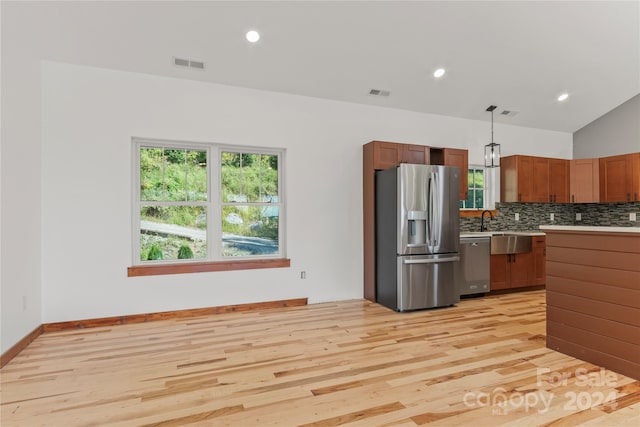 kitchen with lofted ceiling, hanging light fixtures, backsplash, stainless steel appliances, and light hardwood / wood-style floors