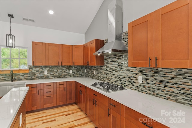 kitchen featuring light wood-type flooring, decorative backsplash, wall chimney exhaust hood, and stainless steel gas cooktop