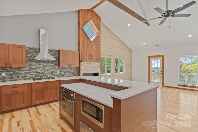 kitchen with decorative backsplash, stainless steel appliances, ceiling fan, light hardwood / wood-style flooring, and wall chimney range hood