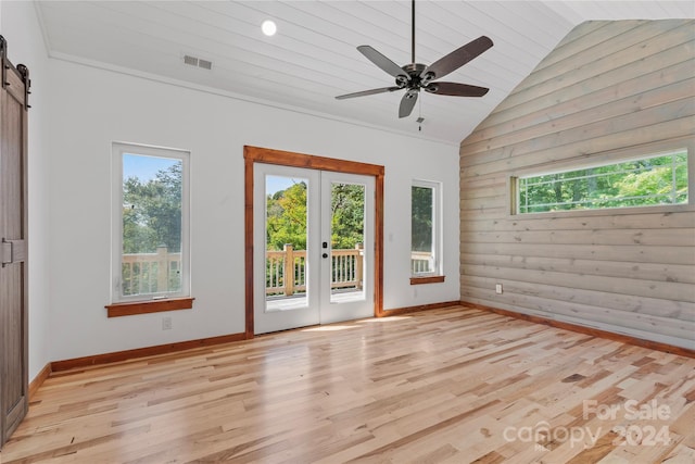 unfurnished room featuring ceiling fan, wooden walls, light hardwood / wood-style flooring, a barn door, and vaulted ceiling