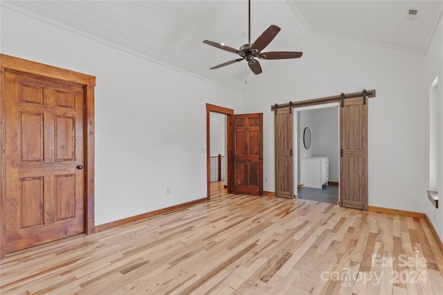 unfurnished bedroom with a barn door, ceiling fan, ensuite bathroom, and light hardwood / wood-style flooring