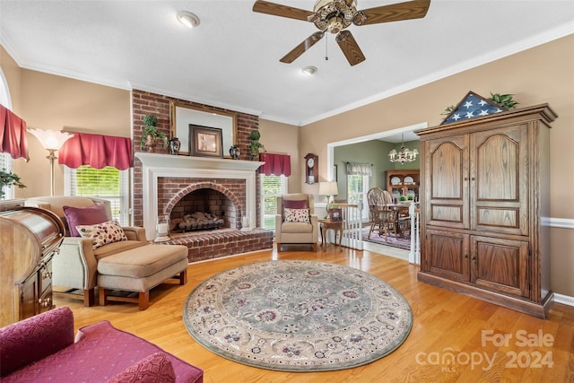 living room featuring ceiling fan with notable chandelier, light hardwood / wood-style floors, ornamental molding, and a brick fireplace