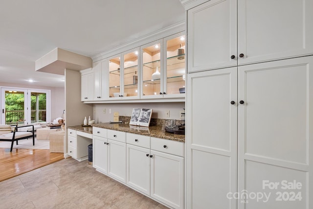 bar featuring light hardwood / wood-style flooring, dark stone counters, built in desk, and white cabinetry