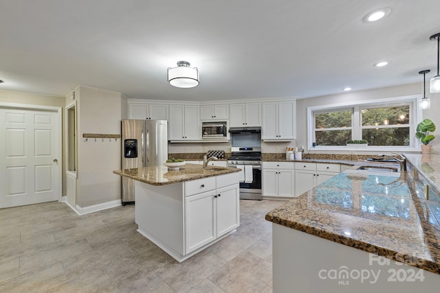 kitchen with white cabinets, pendant lighting, stainless steel appliances, a kitchen island with sink, and sink