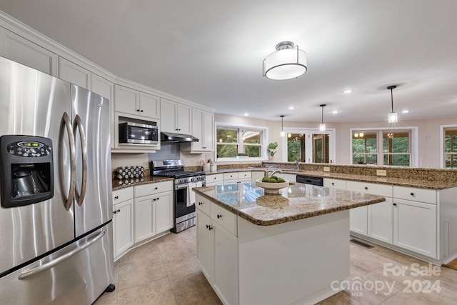 kitchen with pendant lighting, a center island, white cabinets, stainless steel appliances, and light stone countertops