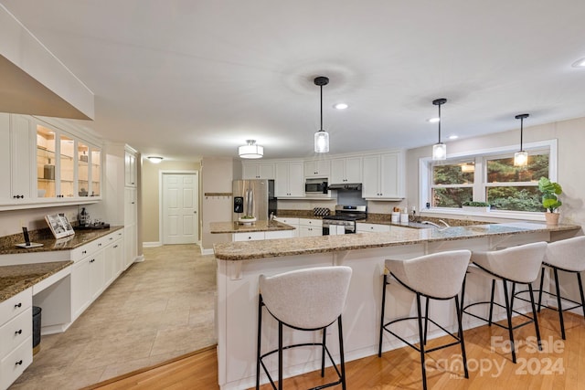 kitchen featuring hanging light fixtures, white cabinets, stone countertops, stainless steel appliances, and light wood-type flooring