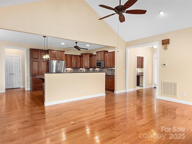 kitchen with stainless steel appliances, decorative light fixtures, a center island, and light hardwood / wood-style flooring