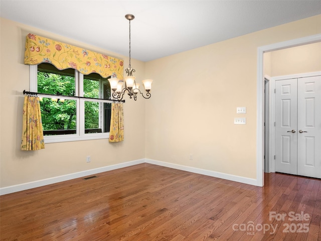 empty room featuring wood-type flooring and a notable chandelier