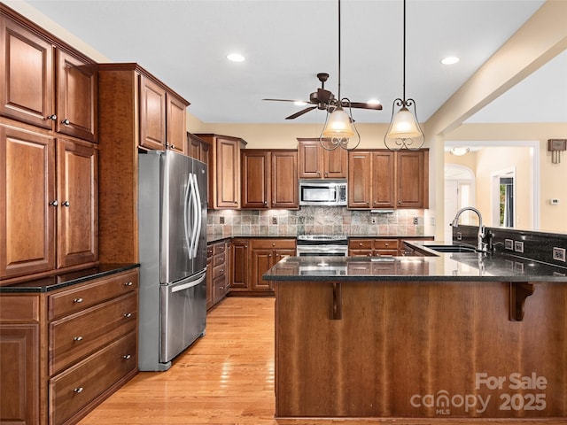 kitchen featuring sink, a breakfast bar area, hanging light fixtures, dark stone counters, and stainless steel appliances