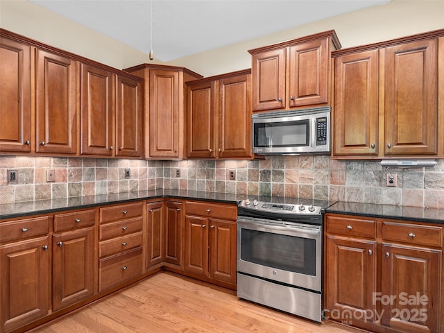 kitchen with tasteful backsplash, appliances with stainless steel finishes, dark stone countertops, and light hardwood / wood-style floors