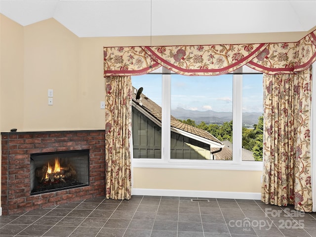 interior space with a mountain view, a fireplace, dark tile patterned flooring, and vaulted ceiling