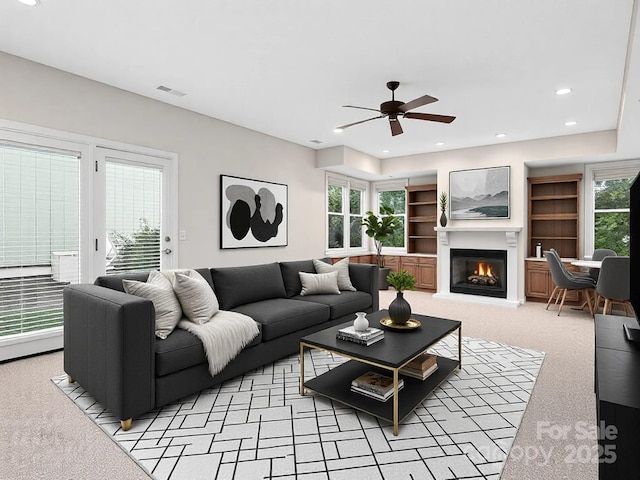 living room with built in shelves, light colored carpet, and ceiling fan