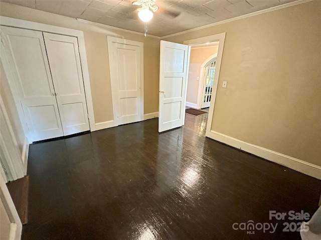 unfurnished bedroom featuring crown molding and dark wood-type flooring