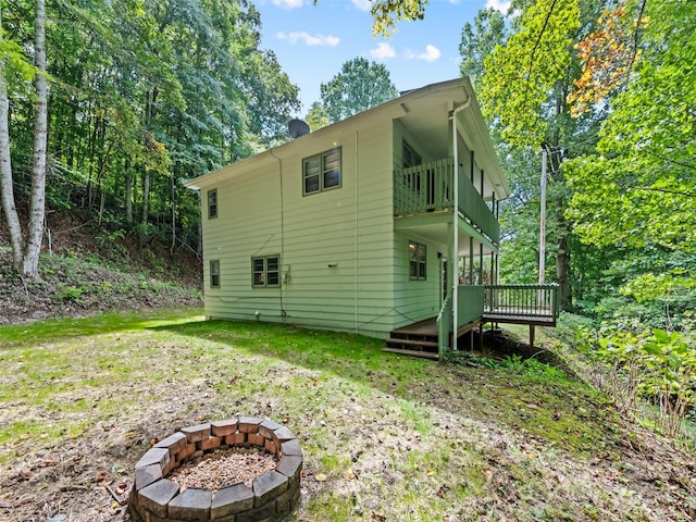 rear view of property with a wooden deck, a yard, a balcony, and a fire pit