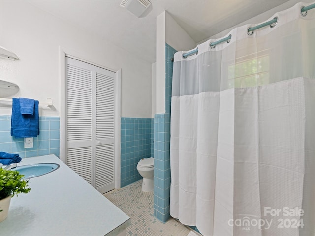 bathroom with tile walls, tile patterned flooring, toilet, vanity, and curtained shower