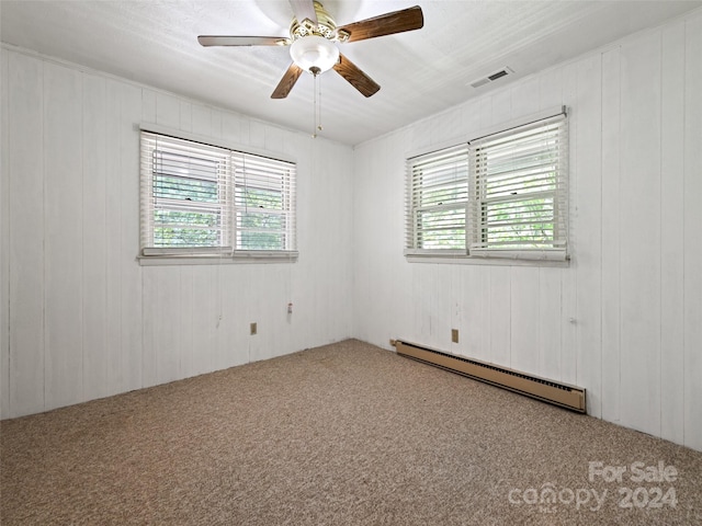 spare room featuring carpet floors, wooden walls, baseboard heating, and ceiling fan