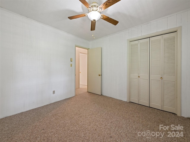 unfurnished bedroom featuring ceiling fan, a closet, light carpet, and wood walls