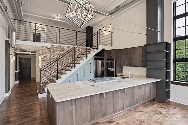 kitchen with stainless steel appliances, a towering ceiling, kitchen peninsula, and dark brown cabinetry