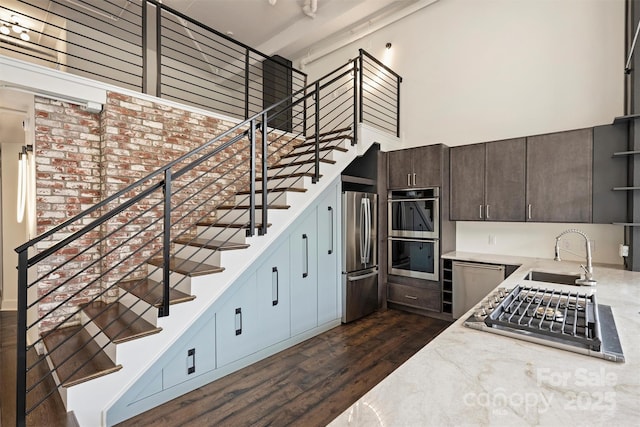 kitchen with appliances with stainless steel finishes, a towering ceiling, dark wood-type flooring, dark brown cabinetry, and sink