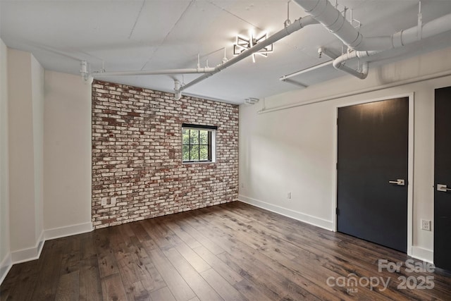 spare room featuring brick wall and dark hardwood / wood-style floors